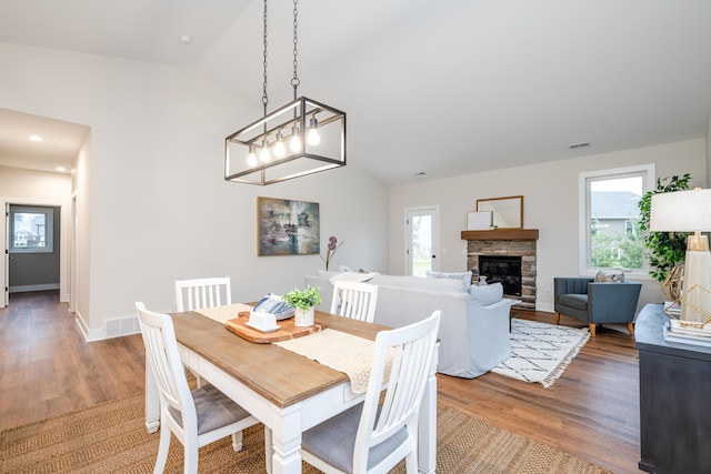 dining area with hardwood / wood-style floors, vaulted ceiling, and a stone fireplace