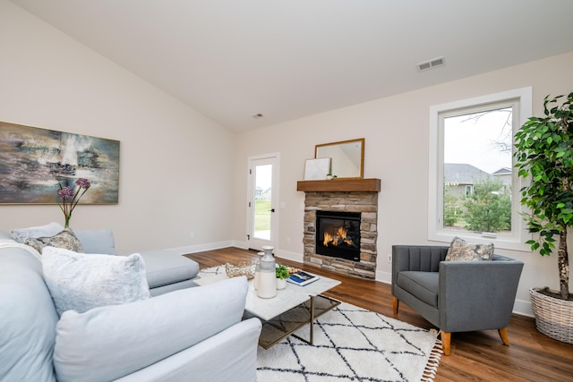 living room with hardwood / wood-style flooring, a stone fireplace, and vaulted ceiling