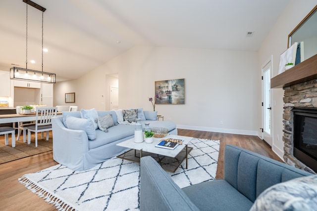 living room featuring wood-type flooring, vaulted ceiling, and a stone fireplace