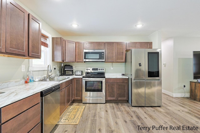 kitchen featuring light stone countertops, stainless steel appliances, light hardwood / wood-style flooring, and sink