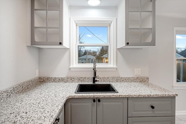 kitchen with gray cabinetry, light stone counters, and sink