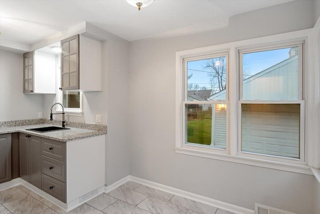 kitchen with gray cabinetry, light stone countertops, and sink