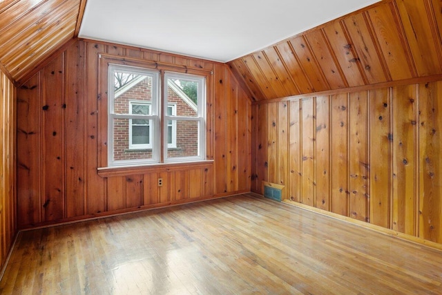 additional living space with wood walls, lofted ceiling, and light wood-type flooring