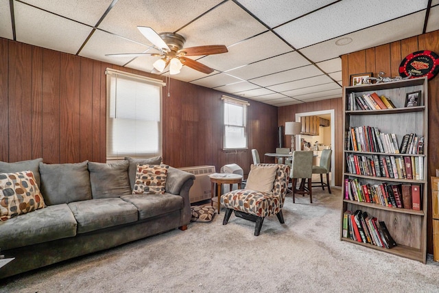 carpeted living room featuring a paneled ceiling, ceiling fan, and wood walls