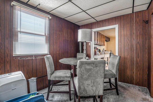 dining space featuring a drop ceiling, wood walls, and carpet floors