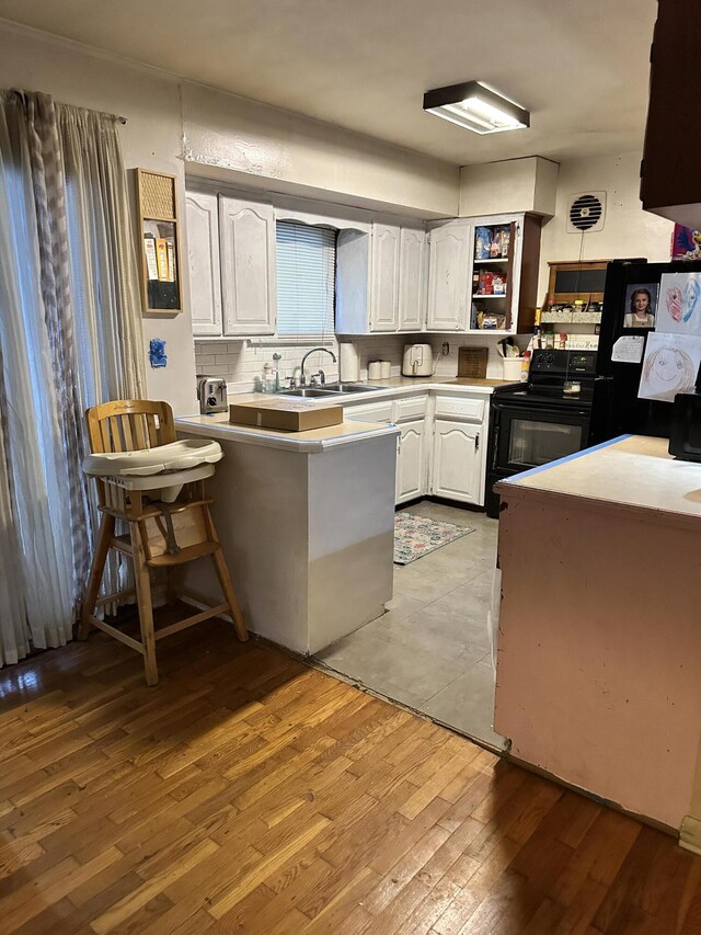 kitchen with black appliances, kitchen peninsula, light hardwood / wood-style floors, a kitchen bar, and white cabinetry