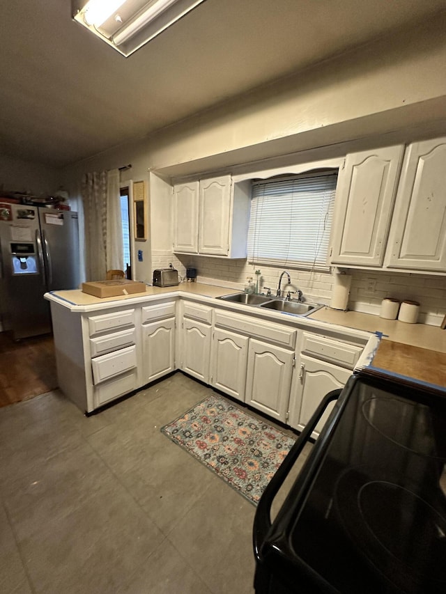 kitchen featuring kitchen peninsula, stainless steel fridge, white cabinetry, and sink