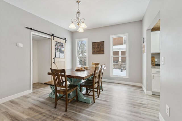 dining area with a barn door, light hardwood / wood-style flooring, and an inviting chandelier