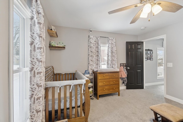 bedroom featuring ceiling fan, light colored carpet, a crib, and multiple windows