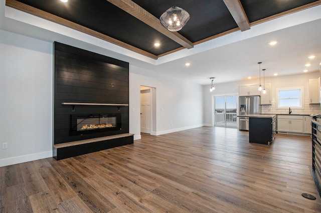 unfurnished living room with beamed ceiling, wood-type flooring, a large fireplace, and sink