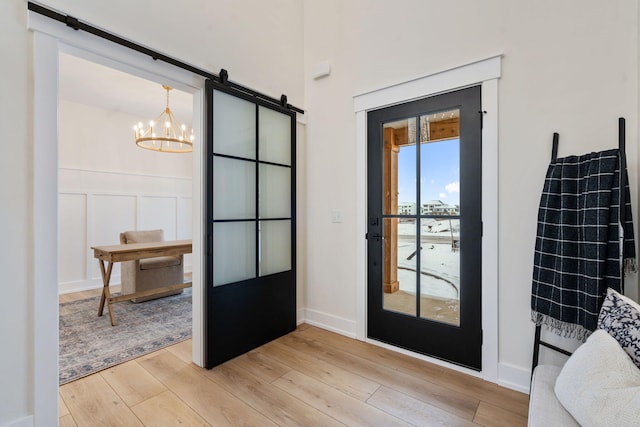 doorway to outside with a notable chandelier, light hardwood / wood-style floors, and a barn door