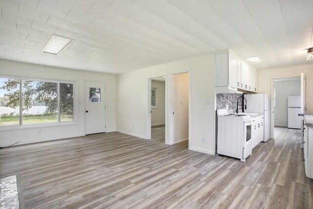 kitchen with stove, tasteful backsplash, light hardwood / wood-style flooring, white fridge, and white cabinetry