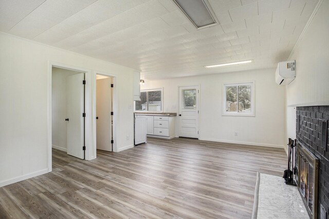 unfurnished living room with a fireplace, light wood-type flooring, a wall unit AC, and crown molding