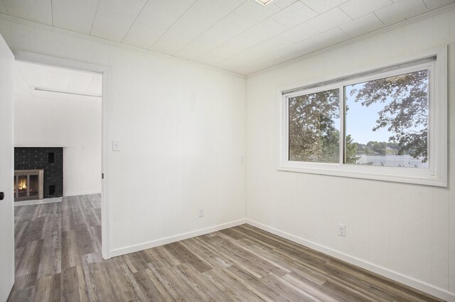 unfurnished room featuring crown molding, wood-type flooring, and a brick fireplace