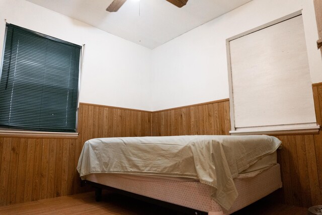 bedroom with ceiling fan, wood-type flooring, and wooden walls