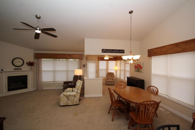 dining space featuring ceiling fan with notable chandelier, carpet floors, and vaulted ceiling