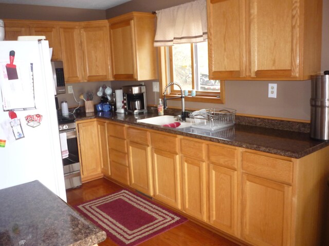 kitchen featuring sink, dark hardwood / wood-style flooring, stainless steel appliances, and dark stone counters