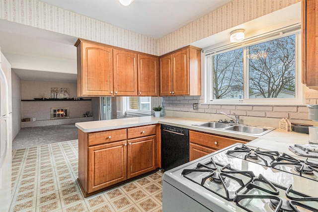 kitchen with dishwasher, sink, a brick fireplace, white gas range, and kitchen peninsula