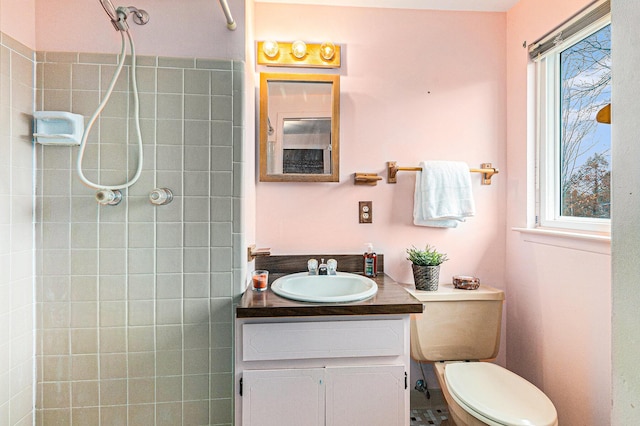 bathroom with a tile shower, plenty of natural light, vanity, and toilet