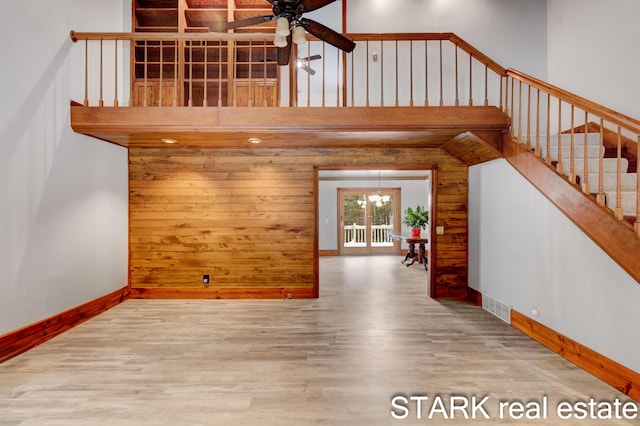 unfurnished living room with a towering ceiling, wood-type flooring, and ceiling fan with notable chandelier