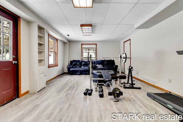 workout room featuring a wealth of natural light, a drop ceiling, built in features, and light wood-type flooring