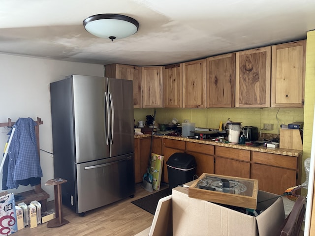 kitchen featuring light wood-type flooring, tasteful backsplash, stainless steel refrigerator, and light stone counters