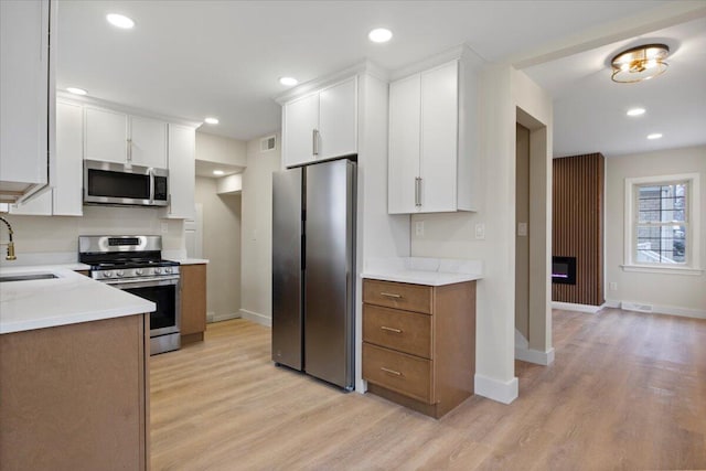 kitchen featuring light stone countertops, white cabinetry, sink, light hardwood / wood-style floors, and appliances with stainless steel finishes