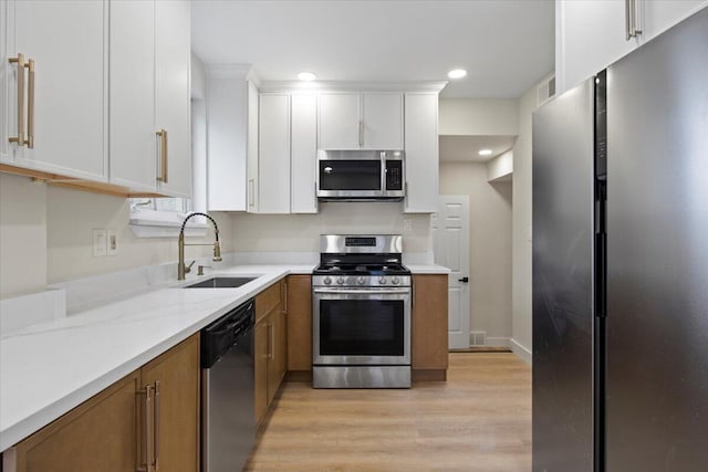 kitchen with light stone countertops, sink, stainless steel appliances, light hardwood / wood-style flooring, and white cabinets