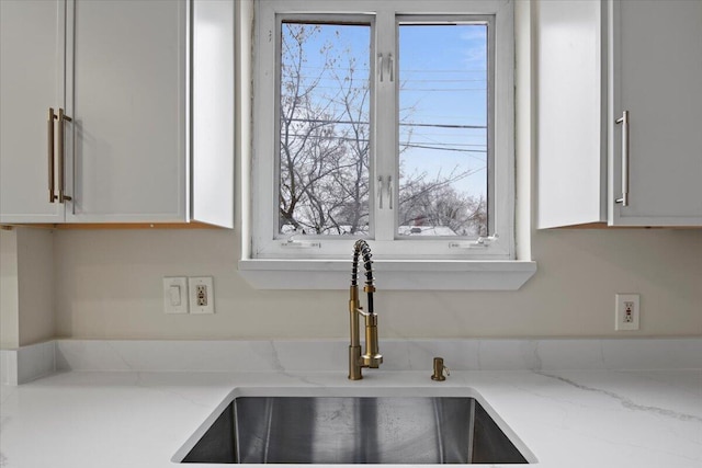 room details featuring light stone countertops, white cabinetry, and sink