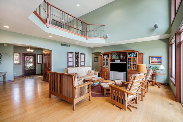 living room with an inviting chandelier, a high ceiling, and light wood-type flooring