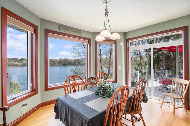 dining area with light hardwood / wood-style floors, a water view, and an inviting chandelier