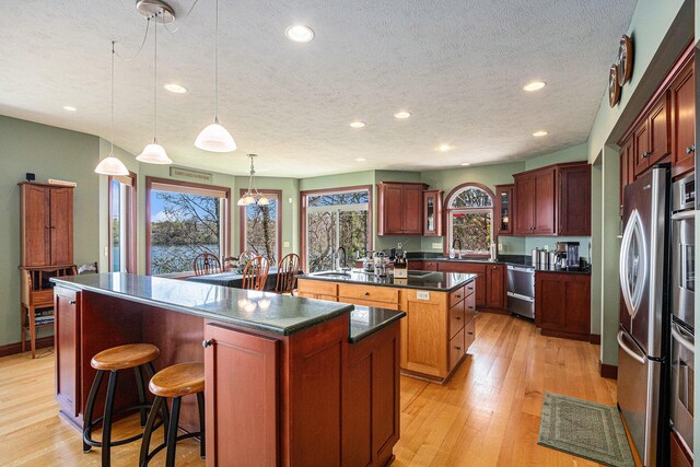 kitchen with light wood-type flooring, a textured ceiling, stainless steel appliances, a center island, and hanging light fixtures