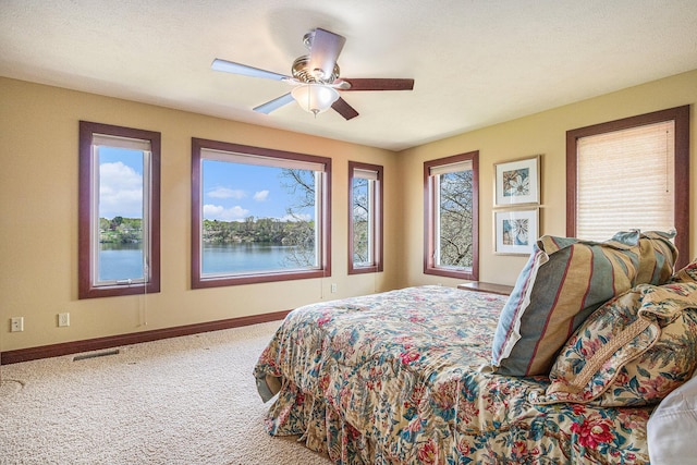 bedroom with carpet flooring, ceiling fan, a water view, and multiple windows