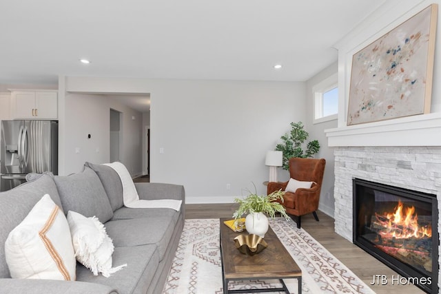 living area with recessed lighting, a stone fireplace, baseboards, and wood finished floors