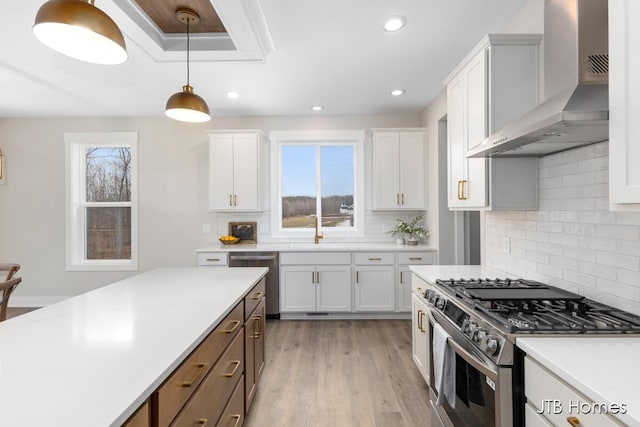 kitchen featuring light wood-style flooring, stainless steel appliances, white cabinetry, hanging light fixtures, and wall chimney exhaust hood