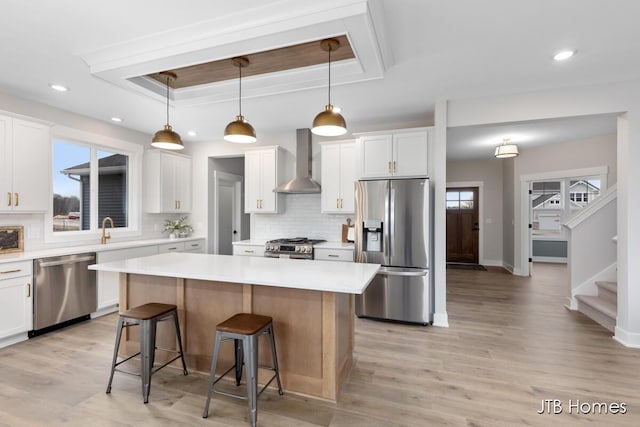 kitchen featuring a kitchen island, a kitchen breakfast bar, appliances with stainless steel finishes, wall chimney exhaust hood, and a raised ceiling