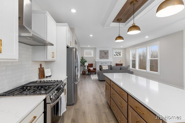 kitchen featuring white cabinets, wall chimney range hood, stainless steel appliances, and light countertops