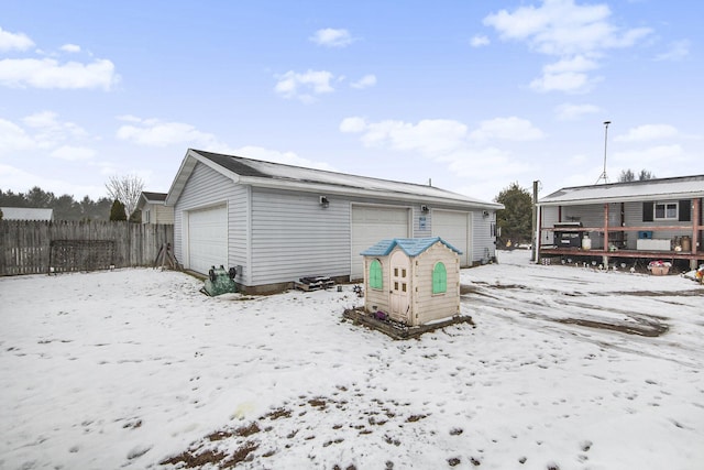 snow covered rear of property featuring a garage and an outbuilding