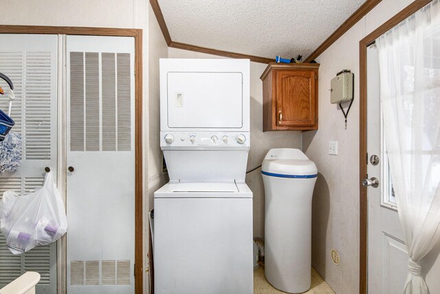 laundry area featuring stacked washer / dryer, cabinets, a textured ceiling, and ornamental molding