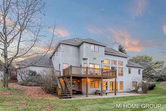 back house at dusk with a lawn, a patio, and a deck