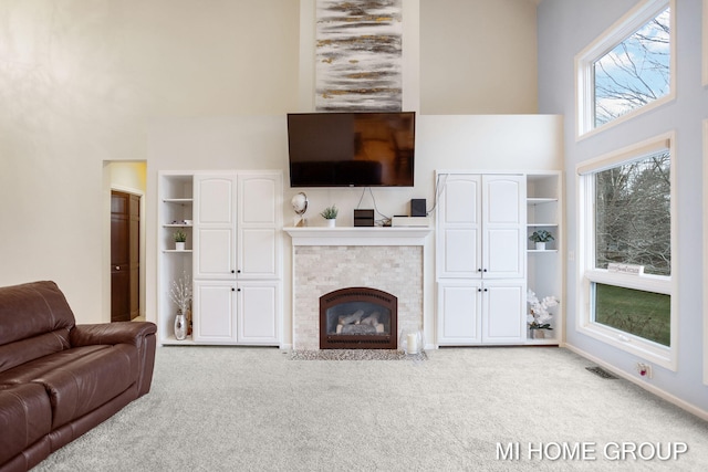 carpeted living room featuring built in features, a high ceiling, and a tiled fireplace