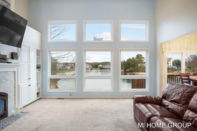 living room featuring light carpet, a high ceiling, plenty of natural light, and a tiled fireplace