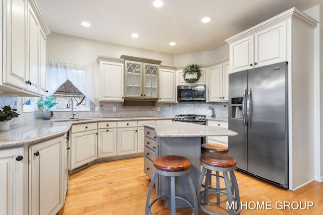 kitchen with light wood-type flooring, stainless steel appliances, sink, white cabinets, and a kitchen island