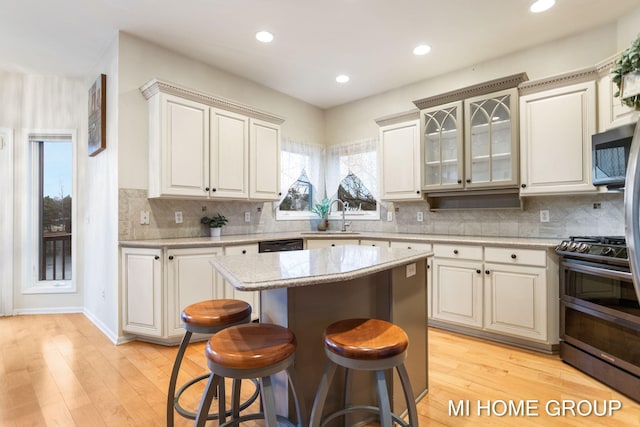 kitchen featuring black stove, sink, backsplash, light hardwood / wood-style floors, and a kitchen island