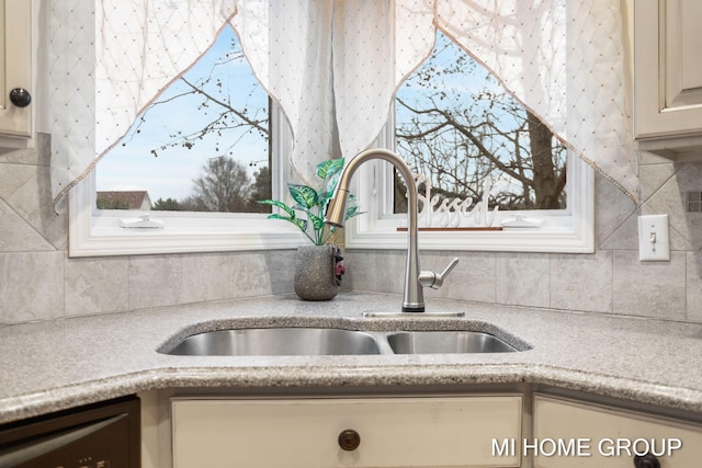 interior details with cream cabinetry, tasteful backsplash, stainless steel dishwasher, and sink