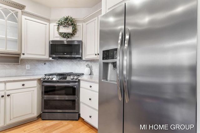 kitchen with tasteful backsplash, light stone countertops, light hardwood / wood-style flooring, and stainless steel appliances