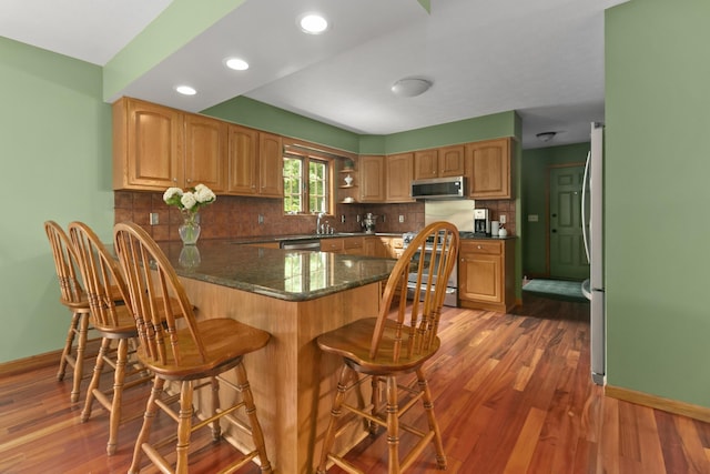 kitchen featuring decorative backsplash, dark hardwood / wood-style flooring, a kitchen bar, kitchen peninsula, and stainless steel appliances