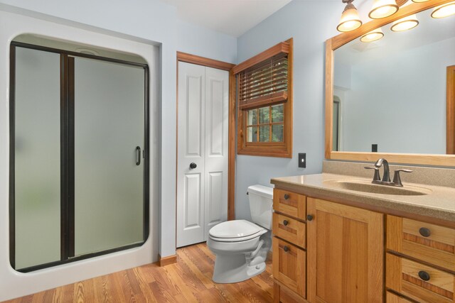 bathroom with hardwood / wood-style floors, vanity, toilet, and a shower with shower door