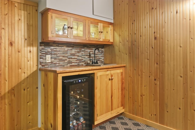 bar featuring tasteful backsplash, beverage cooler, wooden walls, and sink