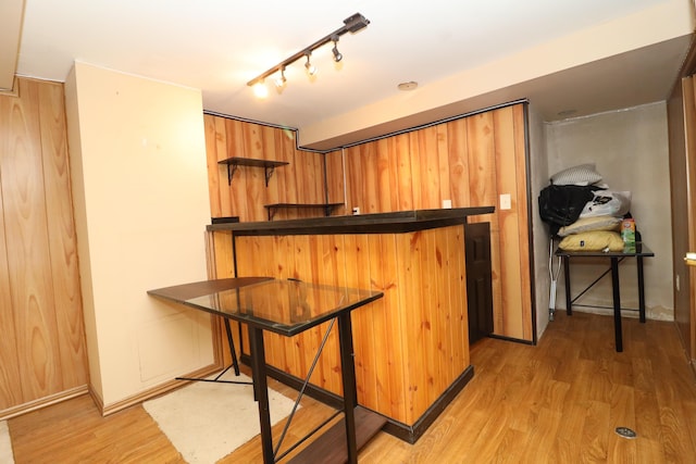 kitchen with kitchen peninsula, a kitchen bar, light wood-type flooring, rail lighting, and wood walls